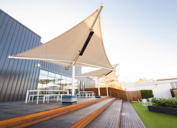 Modern outdoor seating area with large shade umbrellas and wooden decking next to a building.